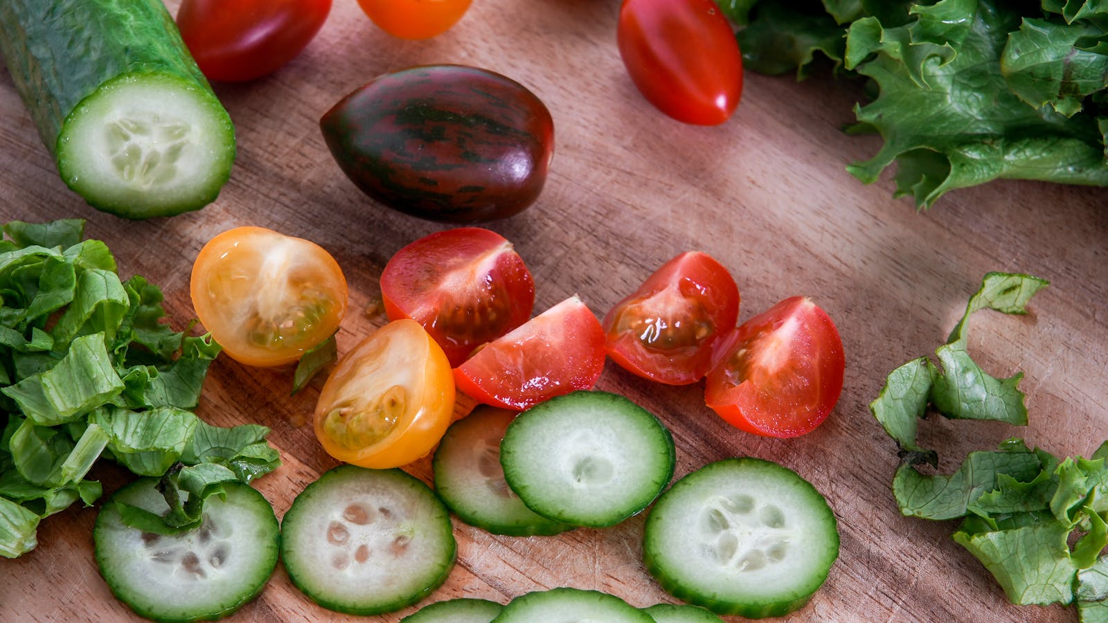 A vibrant assortment of fresh vegetables sliced on a wooden cutting board, perfect for healthy salads.