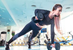 Woman performing a plank row with dumbbells in a bright Dubai gym.