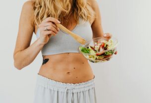 Young woman in sports attire holding a fresh salad bowl, promoting a healthy lifestyle.