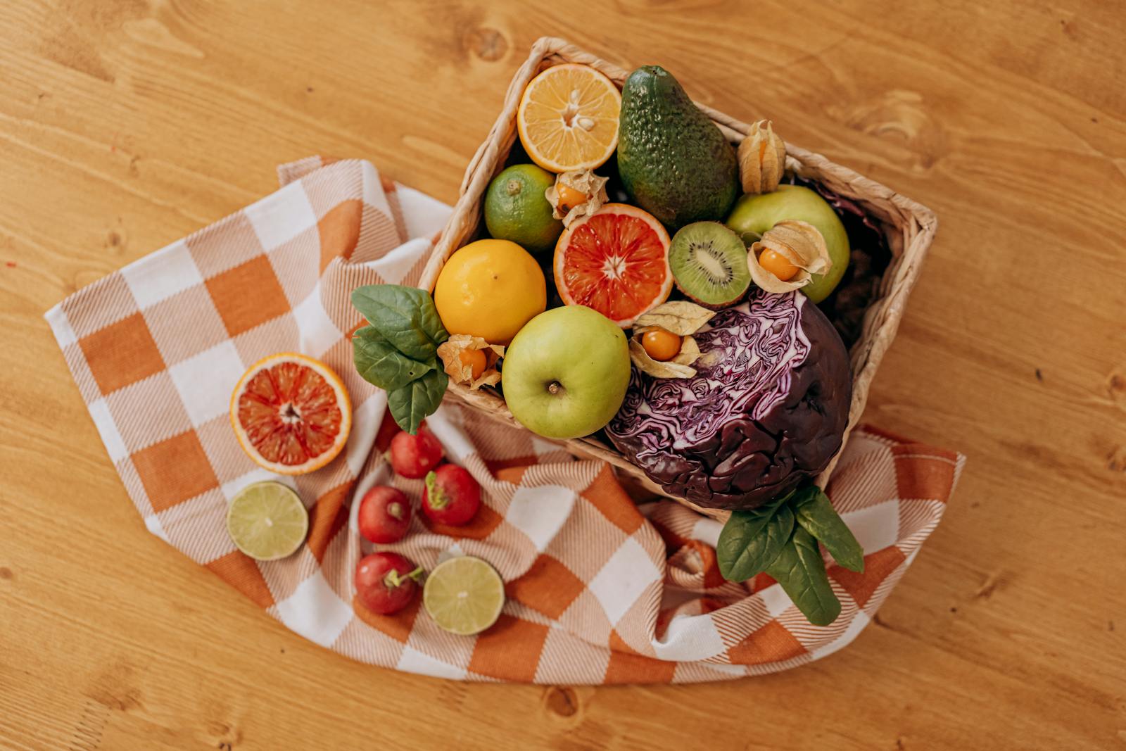 A colorful mix of fruits and vegetables arranged in a basket on a rustic wooden table.