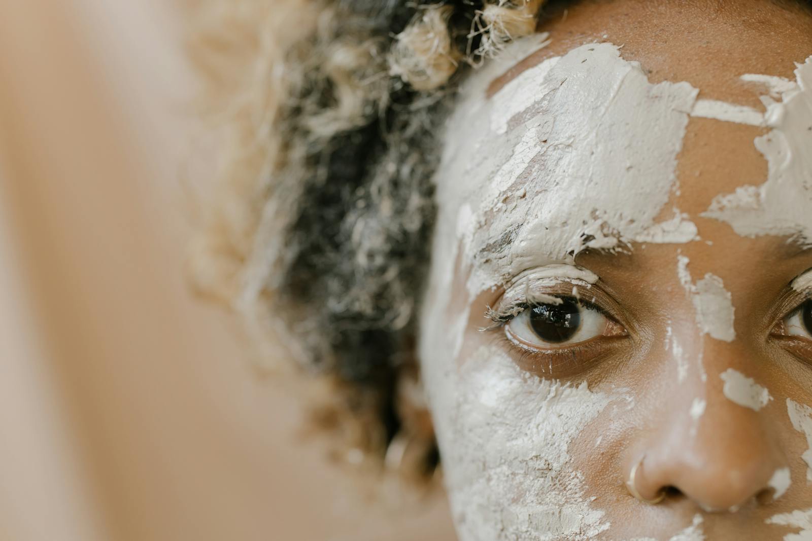 A detailed close-up photo of a person with a facial mud mask applied, focusing on their eye.