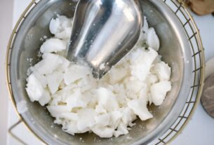 Scooper in a stainless steel bowl filled with chunks of solidified candle wax.