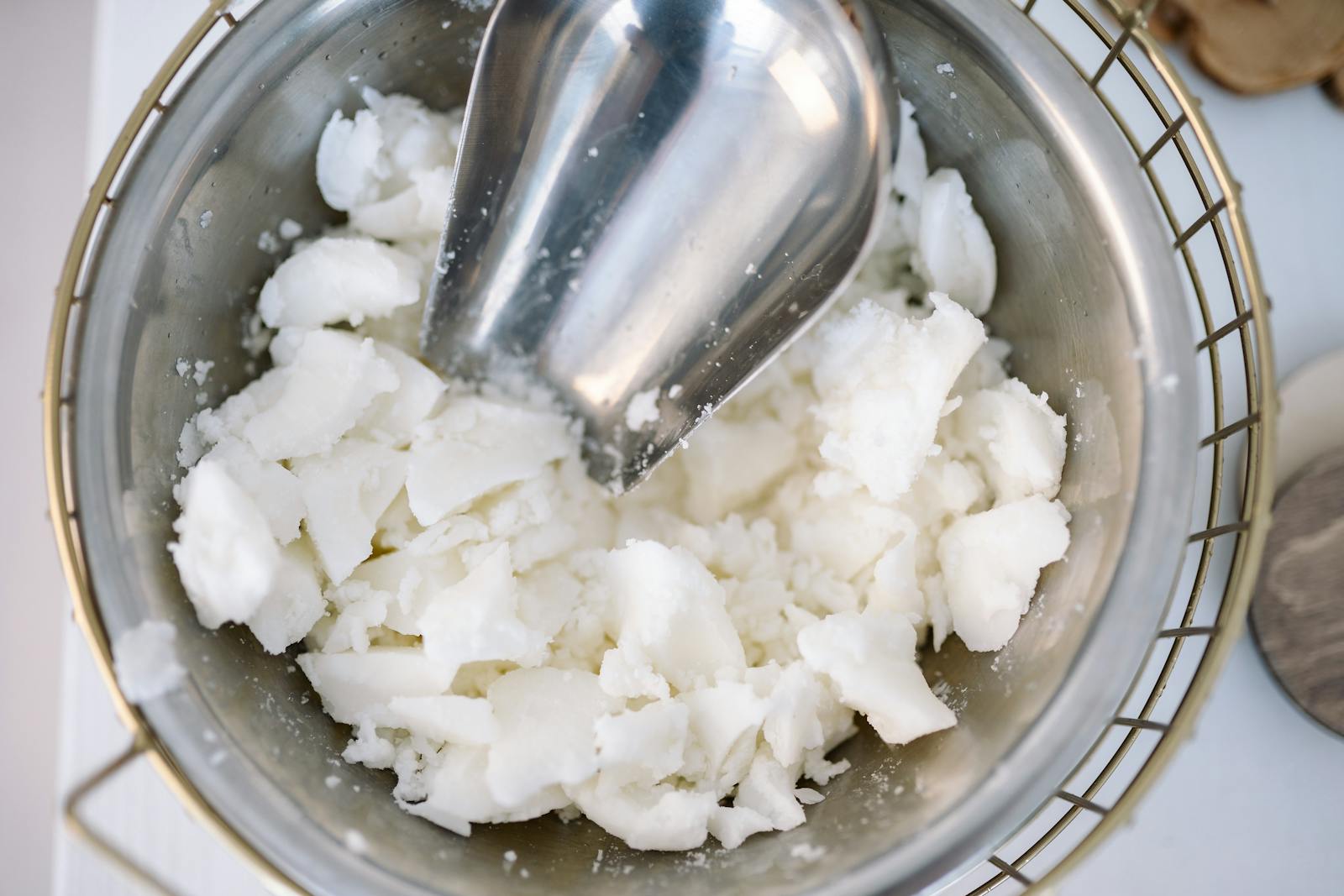 Scooper in a stainless steel bowl filled with chunks of solidified candle wax.