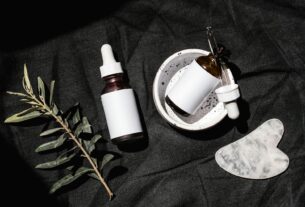 Flat lay of skincare serums and gua sha on black fabric with leaves.