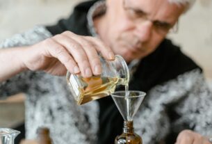 Elderly man carefully decanting liquid into a small bottle with a funnel.